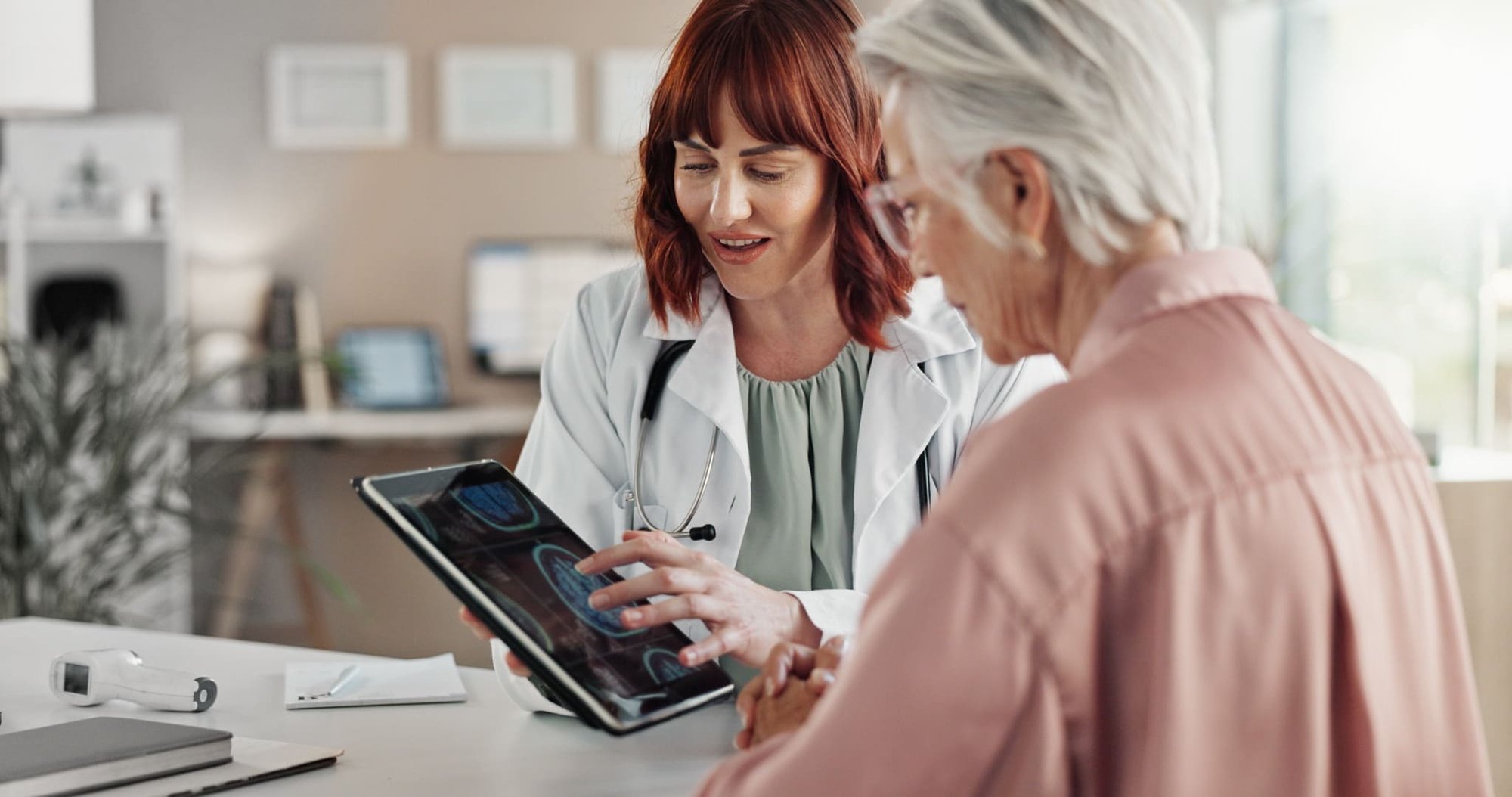 Ärztin zeigt einer Patientin ihre Kopf-Scans auf einem Ipad