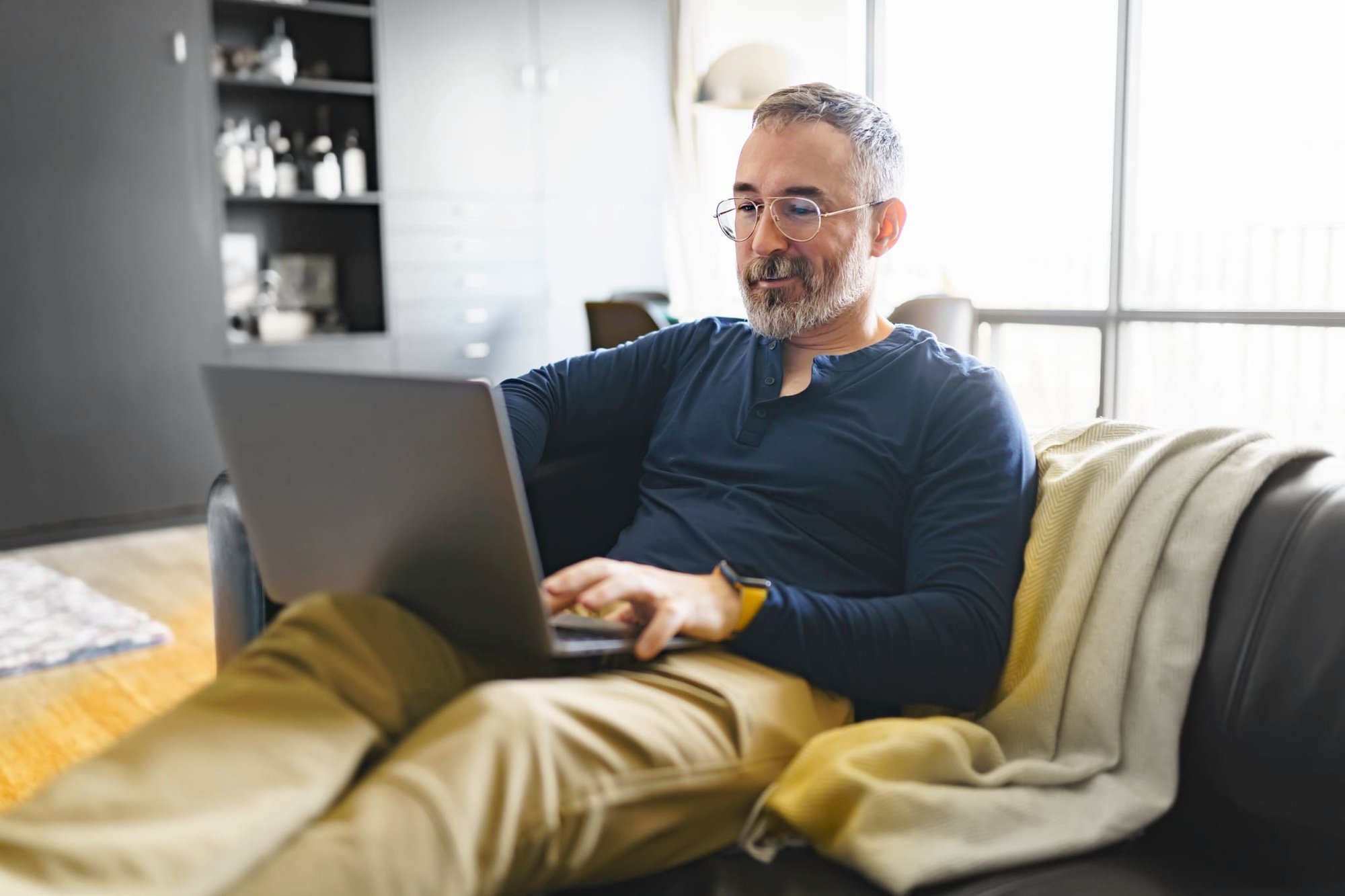 Mann sitzt auf dem Sofa mit einem Laptop auf dem Schoß